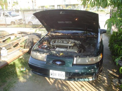 1995 Ford Taurus - 1995 Ford Taurus SHO engine bay with the hood open, parked outdoors.