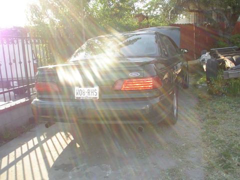 1995 Ford Taurus - The rear of a Ford Taurus is shown with the hood up and sun glare obscuring parts of the image.