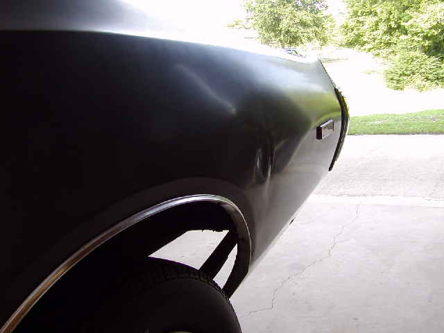 rear quarter panel of a dark-colored car, showing a dent and chrome trim around the wheel well