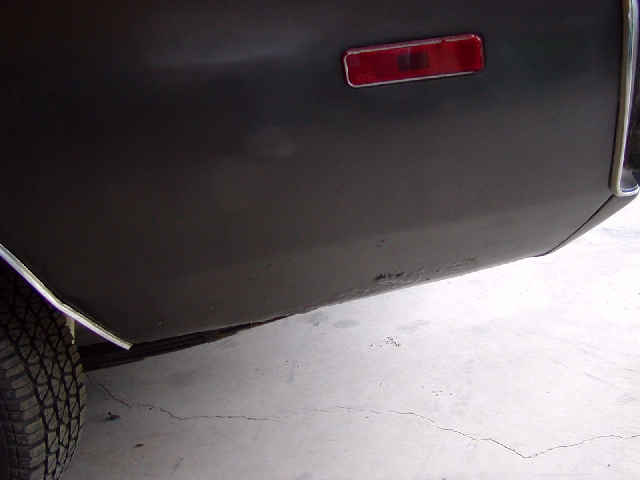 Close-up of dark-colored rear quarter panel with a red reflector and visible rust spots near the bottom edge