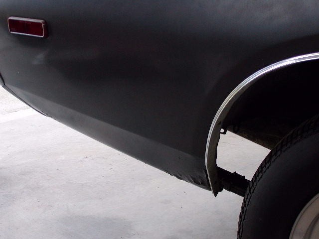 Close-up of a dark colored car's rear quarter panel, showing the taillight and wheel well