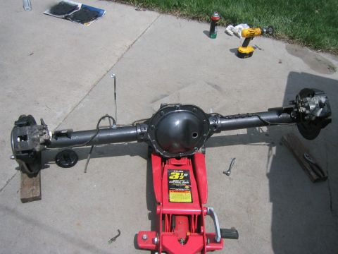 1997 Jeep Cherokee - Rear axle assembly resting on a floor jack with tools and supplies scattered around.