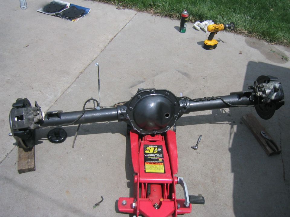 Rear axle assembly on a red 3 1/2 ton floor jack. Tools and spray cans are nearby