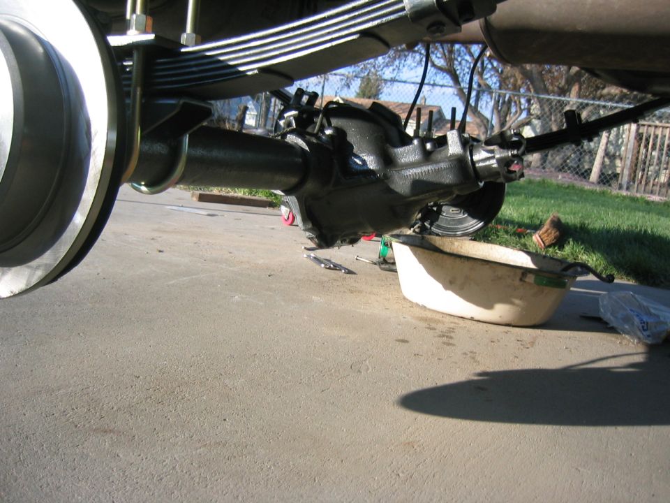 Close-up of a vehicle's rear axle differential with a drain pan underneath. Leaf springs are visible above