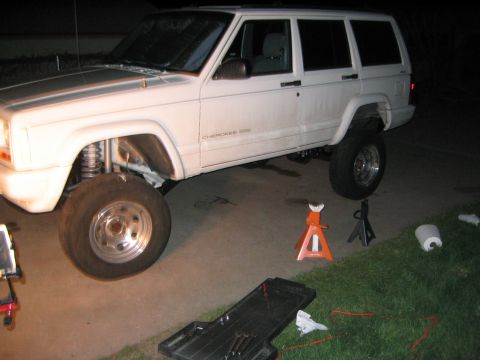 1997 Jeep Cherokee - A white Jeep Cherokee is shown with its front end lifted on jack stands, indicating maintenance or modification work is in progress.