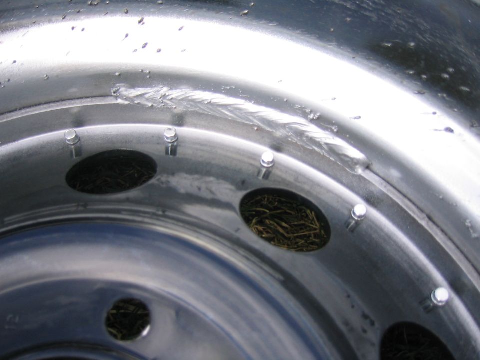 Close-up of a damaged metal wheel rim with visible scratches and debris inside the bolt holes