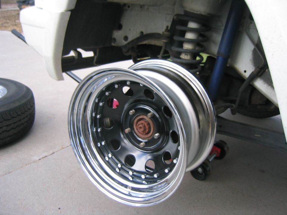 close-up of a shiny custom wheel being installed on a white vehicle, with suspension parts visible