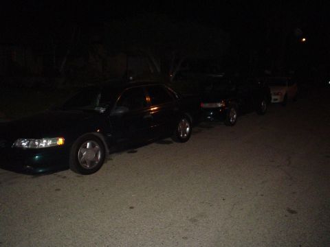 1995 Ford Taurus - Three cars are parked on a street at night, with the closest vehicle appearing to be a 1995 Ford Taurus.