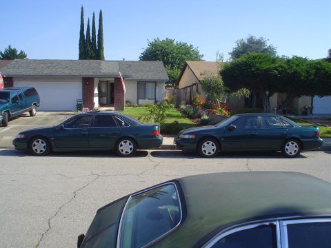 1995 Ford Taurus - Two dark green 1995 Ford Taurus sedans are parked on a residential street.