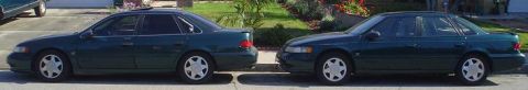 1995 Ford Taurus - Two dark green 1995 Ford Tauruses are parked parallel to each other on a residential street.