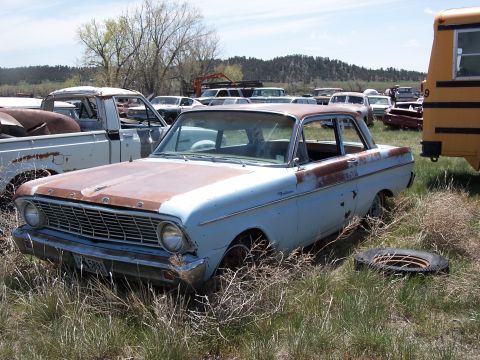 1968 Ford Coupe - A light blue sedan, likely a 1964 model, sits in a junkyard with visible rust on its hood and roof.