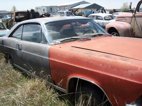 1968 Ford Coupe - This weathered coupe sits in a junkyard, surrounded by other vehicles under a partly cloudy sky.