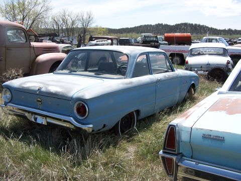 1968 Ford Coupe - Junkyard scene with a light blue sedan parked among other vehicles.