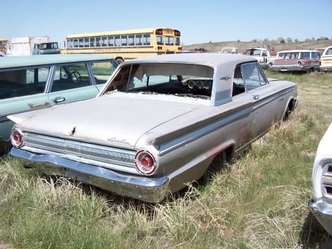 1968 Ford Coupe - This vintage coupe sits in a junkyard, surrounded by other vehicles and overgrown grass under a clear sky.