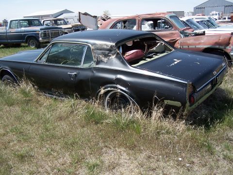 1968 Ford Coupe - Junkyard scene with an abandoned 1967 Mercury Cougar coupe partially hidden by tall grass.
