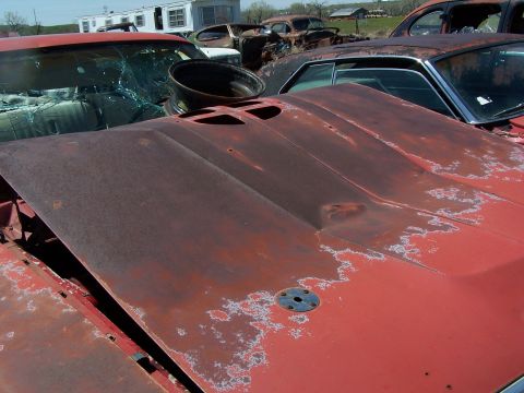 1968 Ford Coupe - A heavily rusted 1968 Ford Coupe sits in a junkyard, its hood showing signs of decay and damage.