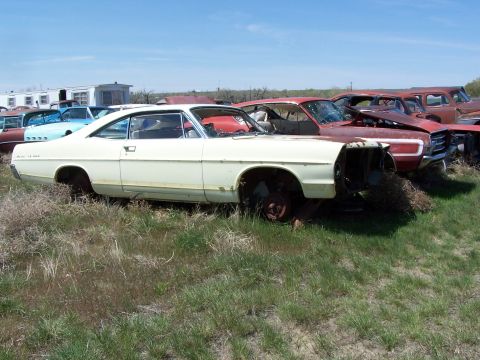 1968 Ford Coupe - A white 1968 Ford Coupe sits in a junkyard, showing its side profile among other vehicles.