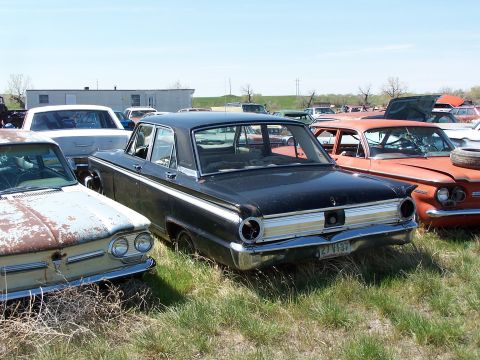 1968 Ford Coupe - A black sedan sits in a junkyard, surrounded by other vehicles under a clear sky.