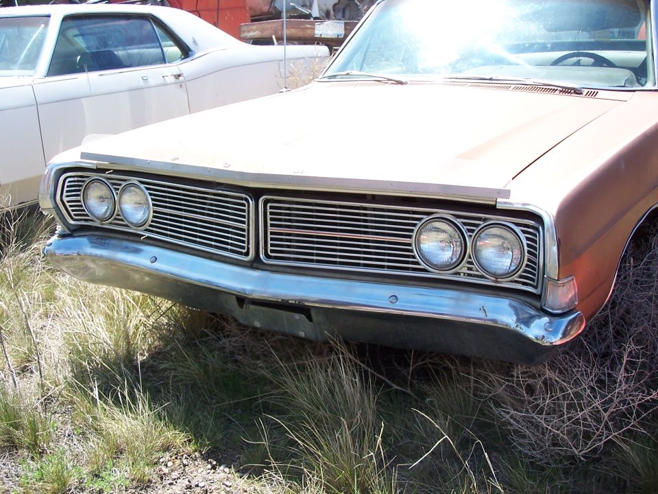Faded copper full-size Ford with quad headlights and chrome bumper in a junkyard
