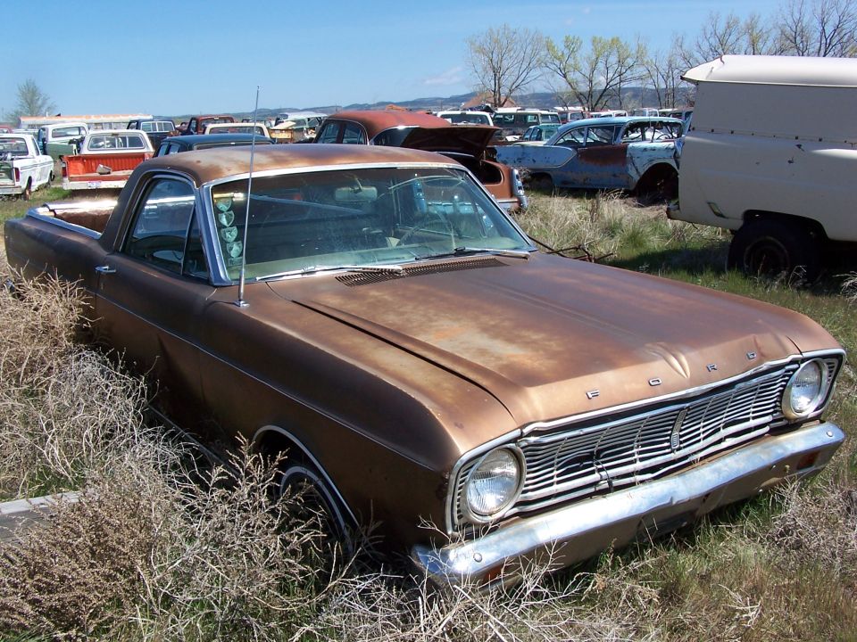 Brown 1968 Ford Ranchero in a junkyard, front 3/4 view, showing rust and overgrown grass