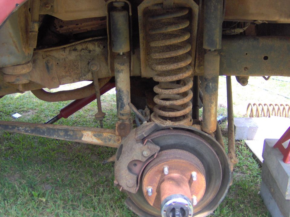 Close-up of rusty rear suspension with coil spring, shock absorber, and brake rotor