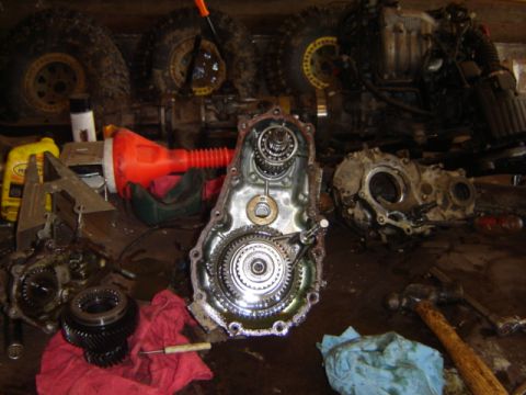 1992 Ford Bronco - Disassembled transfer case components are laid out on a workbench with various tools and tires in the background.