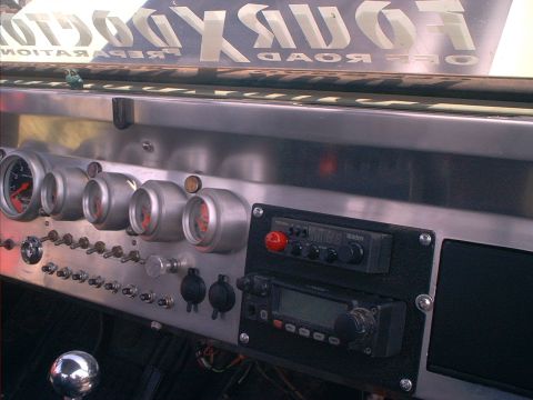 1990 Ford Bronco - Custom brushed-aluminum dash panel viewed across the cab, with a row of five round white-faced gauges, a bank of toggle switches, and two a…