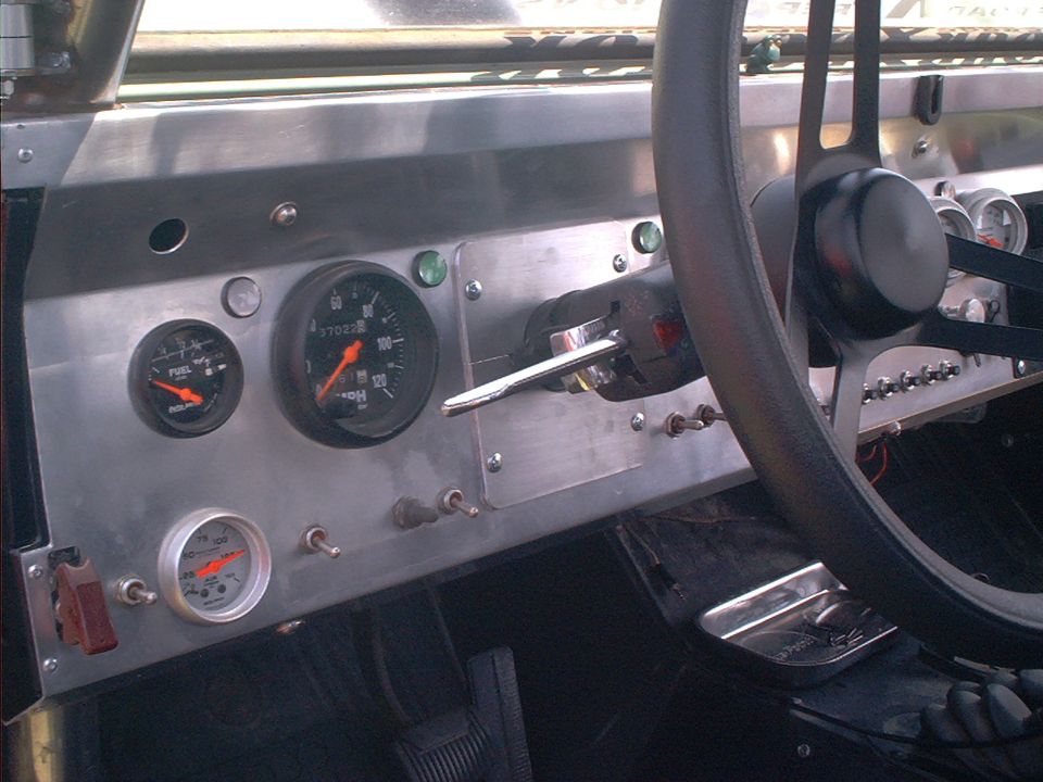 Custom aluminum dash with speedometer, fuel gauge and toggle switches behind a black steering wheel