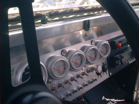 1990 Ford Bronco - Driver's-eye view through the steering wheel at a polished aluminum dash panel carrying Auto Meter oil pressure, water temperature, transmi…
