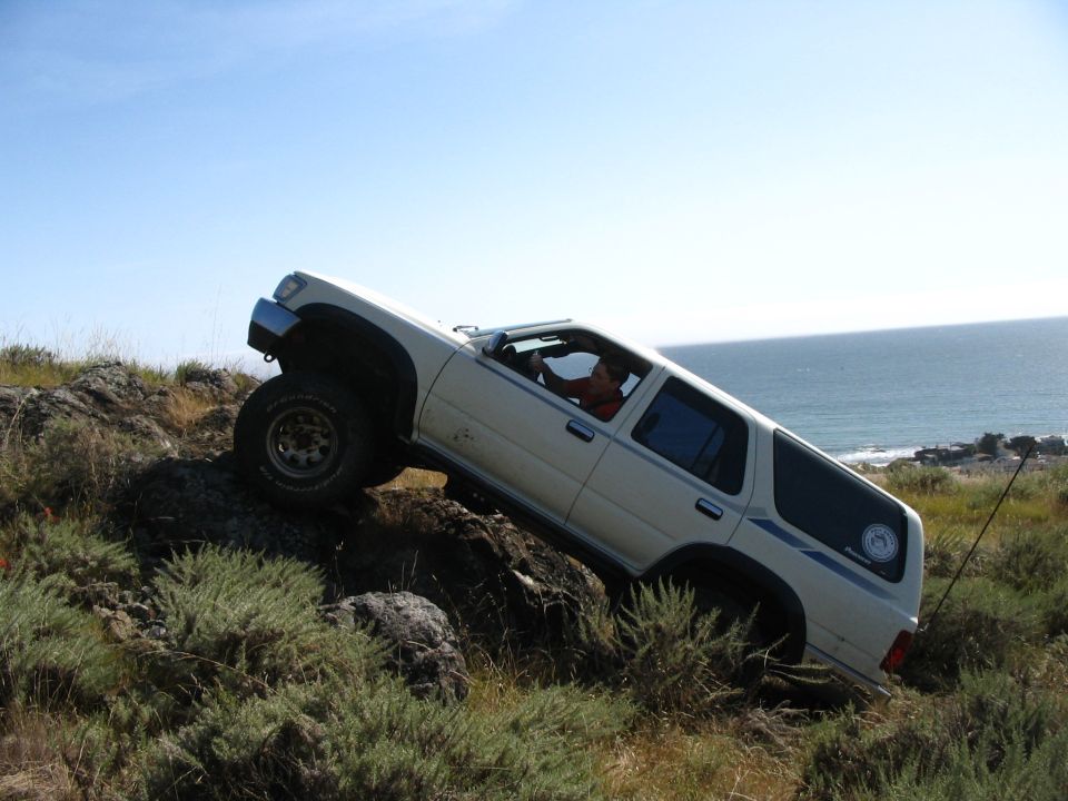 White lifted Toyota 4Runner nose-up on a steep rocky slope above the ocean