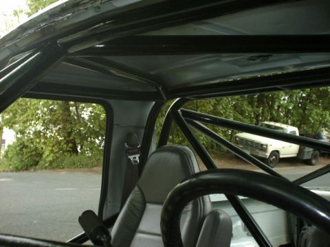 1995 Ford Bronco - Interior view showing a roll cage, with a white flatbed truck visible through the window.