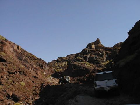 1997 Ford Ranger - Two vehicles navigate a narrow, rocky canyon road under a bright blue sky.