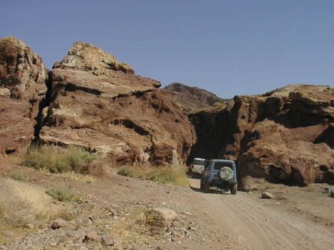 1997 Ford Ranger - Two vehicles navigate a dusty dirt road through a , rocky canyon under a clear blue sky.