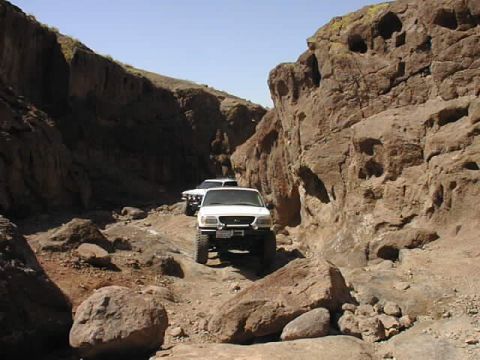 1997 Ford Ranger - Two white trucks drive through a narrow, rocky canyon under a clear blue sky.