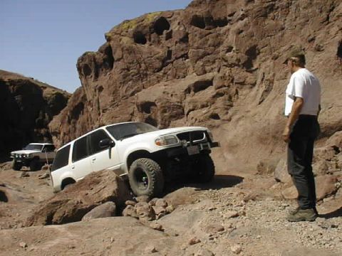 1997 Ford Ranger - Two SUVs tackle a challenging off-road trail in a rocky, desert-like environment.