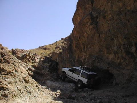 1997 Ford Ranger - White SUV navigates a challenging rocky trail with a large cliff face overhead.