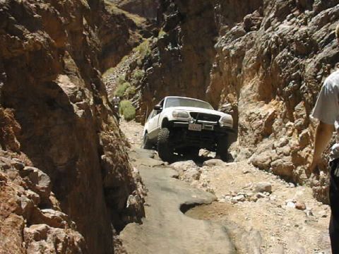 1997 Ford Ranger - A white pickup truck navigates a challenging off-road trail through a narrow canyon.