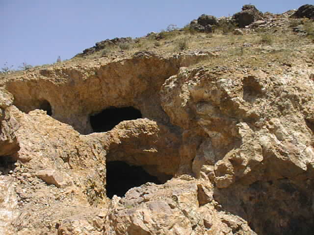 Rocky hillside with several cave openings under a clear blue sky
