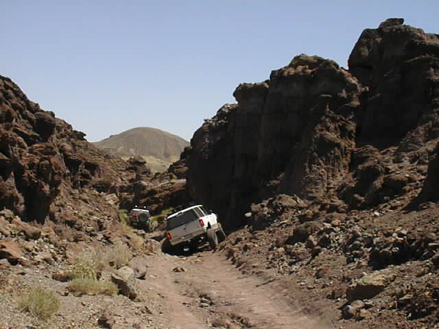 White SUV navigating a rocky canyon road, another vehicle behind