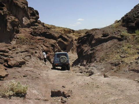 1997 Ford Ranger - A blue SUV navigates a narrow, rocky canyon road under a clear blue sky.