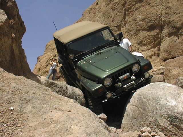 Green Jeep Wrangler navigating a rocky canyon with two people nearby