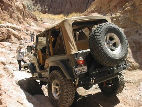 1997 Ford Ranger - A black Jeep Wrangler navigates a narrow, rocky canyon trail with people walking nearby.
