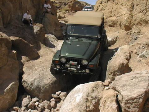 1997 Ford Ranger - A green Jeep Wrangler tackles a challenging rocky path, with spectators observing from the side.