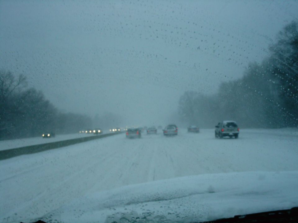 Cars driving on a snow-covered highway with trees on the sides