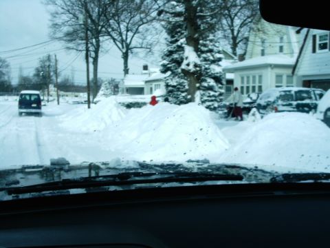 1989 Ford Bronco - A dark SUV navigates a snow-covered street, with houses and snowdrifts lining the road.
