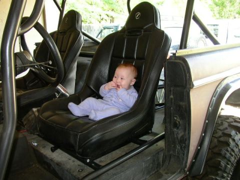 1995 Ford Bronco - A baby sits in a racing seat within a vehicle that has a roll cage.