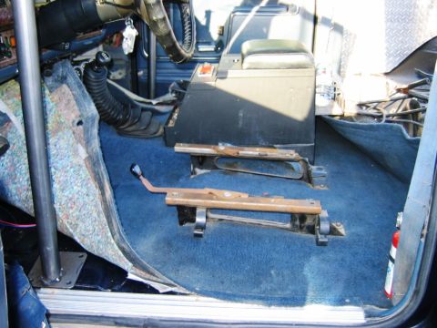 1985 Ford Bronco - The interior of this vehicle shows exposed seat mounting brackets and blue carpeting, with a roll cage visible.