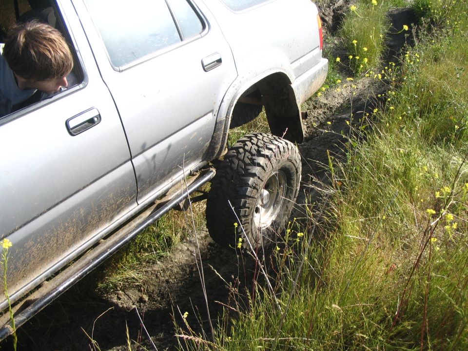 Boy looks out window of a muddy silver lifted 4Runner stuck in a grassy rut
