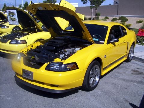 2002 Ford Mustang - A bright yellow 2002 Ford Mustang is displayed with its hood open, revealing the engine, alongside another similar vehicle.