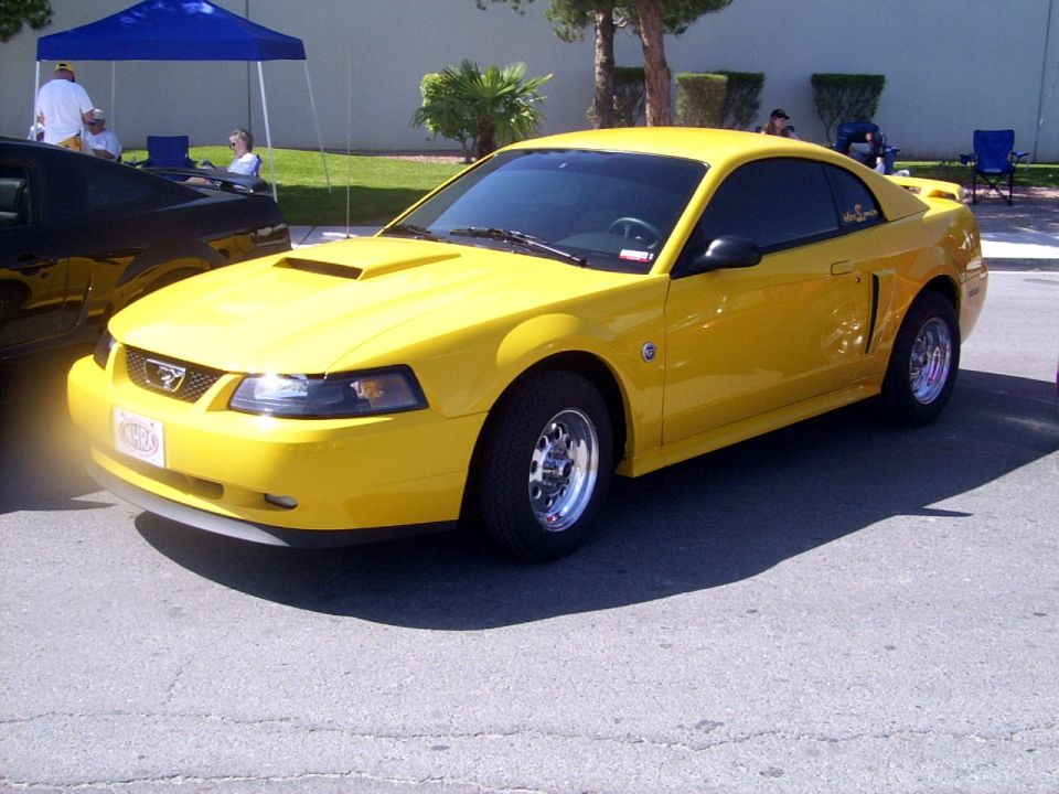 Yellow 2002 Ford Mustang parked next to a black car under a blue tent